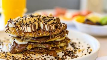 A stack of pancakes with chocolate sauce and crumbled cookies on a white plate.