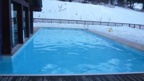 A swimming pool with a wooden deck, surrounded by snow. - Apartment in 4 * residence, Les Alpages de Val Cenis (Lanslevillard)