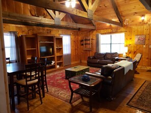 A cozy wooden cabin interior with a dining area, a sofa, a television, and a fireplace. - Cozy waterfront cabin on 20 acres (Wiggins)