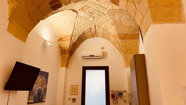 A room with a stone ceiling, an air conditioning unit, a door, and a wall-mounted artwork. - Dimora Giulietta Standard Apartment (Lecce)