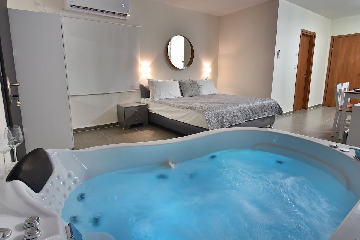Une chambre à coucher avec une grande baignoire, un lit avec des oreillers, une table de chevet et un miroir au mur.