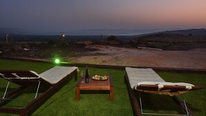 Un salon de plage avec deux chaises longues et une table sur laquelle se trouvent des fruits et une bouteille.