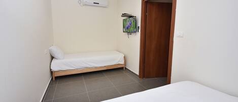 A small, clean room with a single bed, a wooden door, and a mounted TV.
