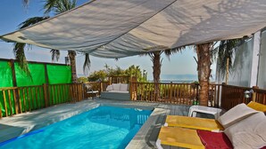 Un espace piscine avec des chaises longues, une terrasse en bois et une vue sur la mer.