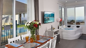 Une chambre moderne dotée d’un coin repas, d’une grande fenêtre offrant une vue sur une piscine et les montagnes, ainsi que d’un jacuzzi.