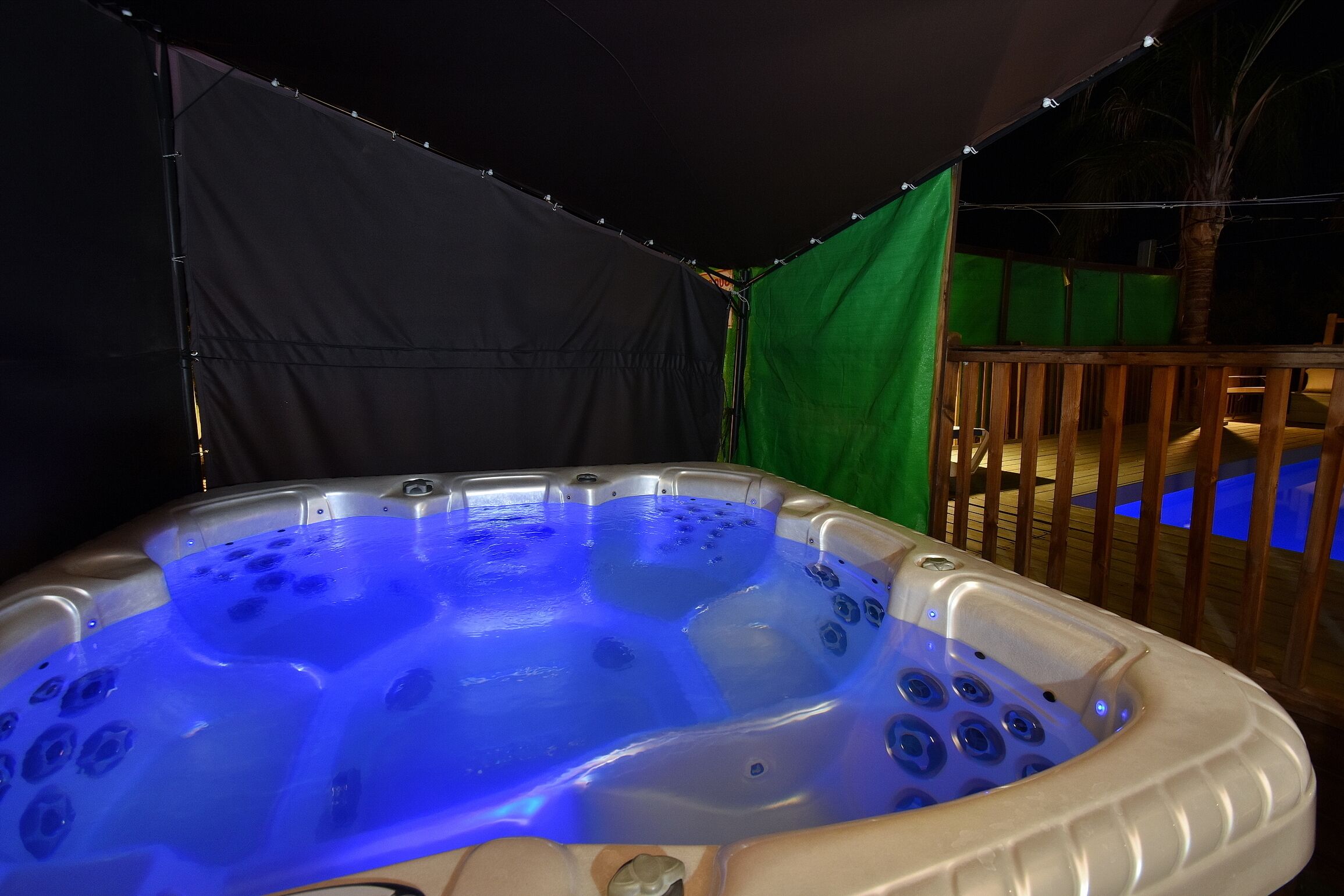 A hot tub with a blue light, surrounded by a wooden deck and a tent.