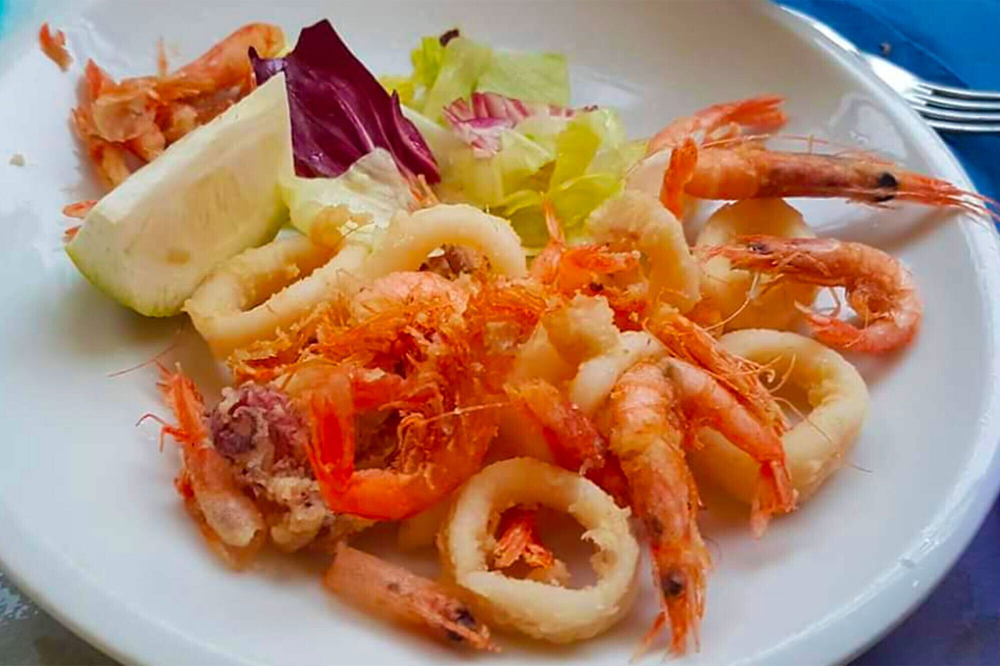 Une assiette de fruits de mer comprenant des crevettes, des rondelles de calamars et une tranche de citron.