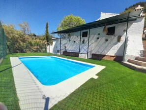 Une piscine dotée d’une terrasse blanche, entourée d’une pelouse artificielle verte.