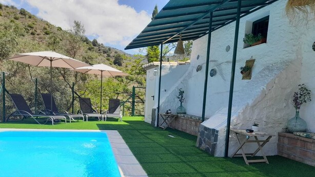 A swimming pool with artificial grass, lounge chairs, and umbrellas.