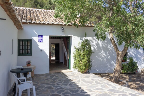 Un bâtiment blanc avec un toit en tuiles, une terrasse en pierre et une porte donnant sur un espace intérieur.