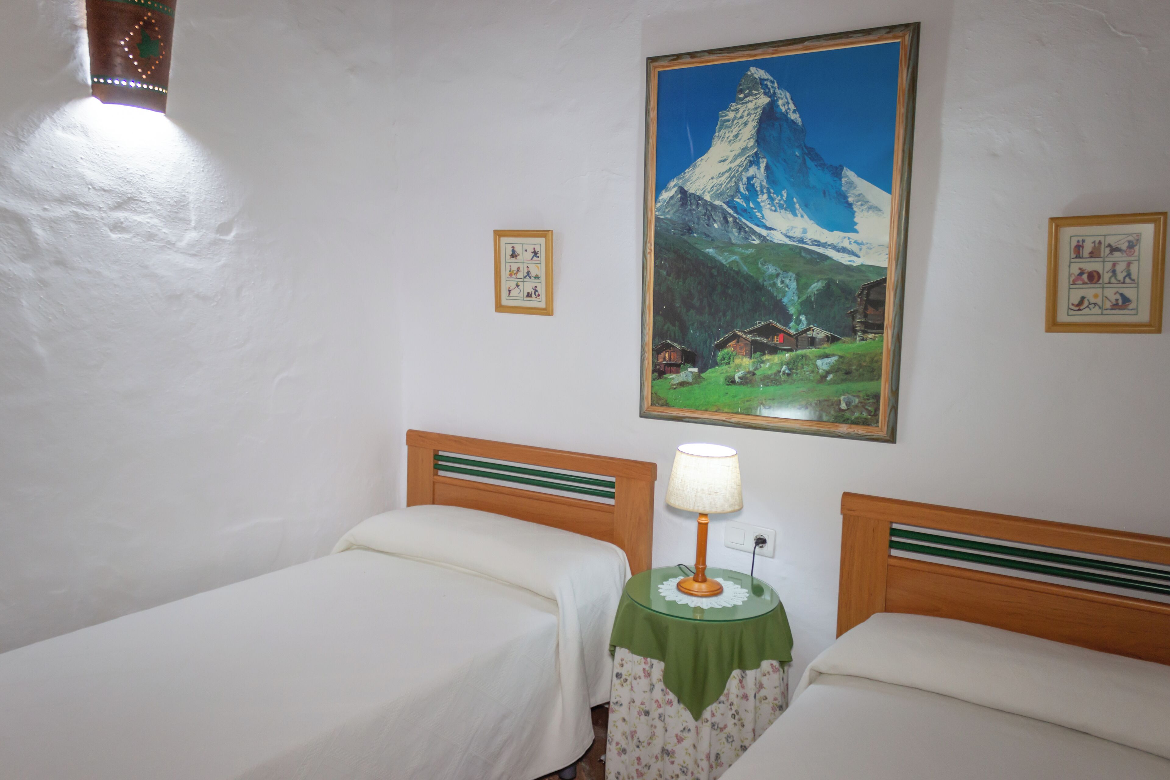 Una habitación con dos camas, un cuadro de una montaña y una mesita con una lámpara.