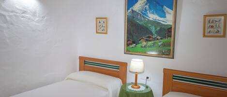 Una habitación con dos camas, un cuadro de una montaña y una mesita con una lámpara.