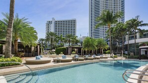 Une piscine entourée d’immeubles imposants, avec des chaises longues et des palmiers.