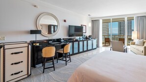 Une chambre d’hôtel comprenant un lit, un bureau avec deux chaises, une télévision, un minibar et une grande fenêtre donnant sur des immeubles.
