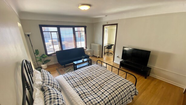 A bedroom with a bed, a TV, a sofa, and a window with blinds.