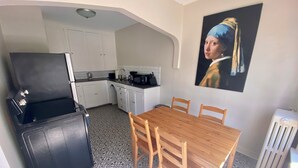 A compact kitchen with white cabinets, a black refrigerator, a wooden dining table with chairs, and a tiled floor.