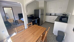 A compact kitchen with a wooden dining table, chairs, a refrigerator, stove, and white cabinets.