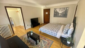 A bedroom with a bed, a television, a radiator, and a small table with a plant.
