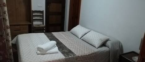 A bedroom with a bed, a wooden wardrobe, a chair, and a small table.