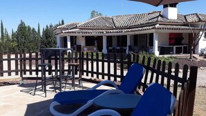Una villa con techo de tejas, zona de estar exterior con sillas y una mesa, y patio amurallado.