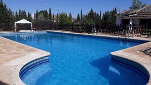 Piscina rectangular con una zona circular de hidromasaje, rodeada por una valla de madera y árboles.
