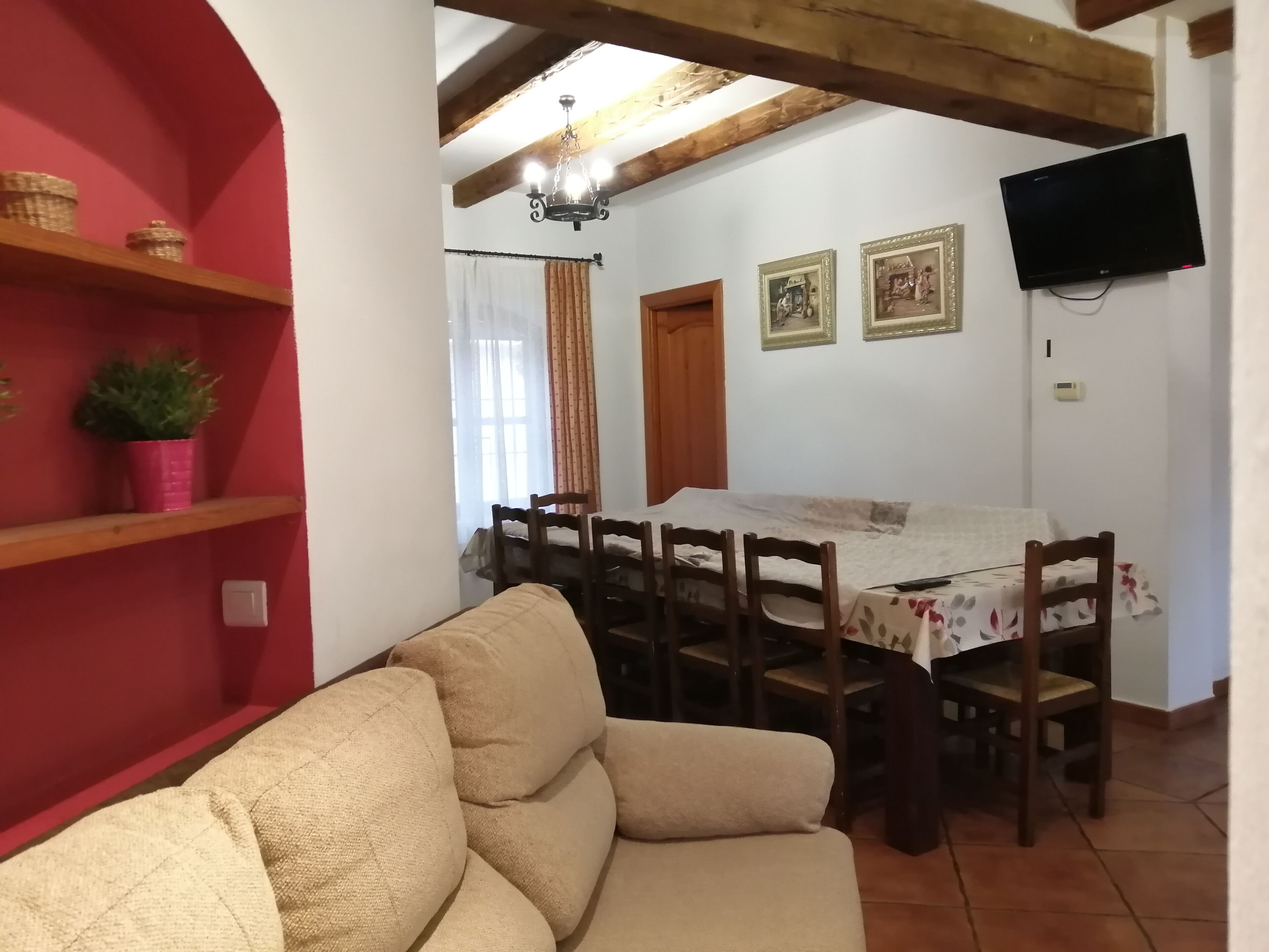 Une pièce chaleureuse avec un canapé, une table à manger et des chaises, un téléviseur fixé au mur et un plafond en bois.