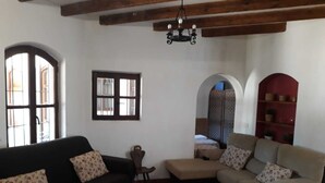 Sala de estar con dos sofás, una mesita y una araña. Hay ventanas y una puerta con un panel decorativo.