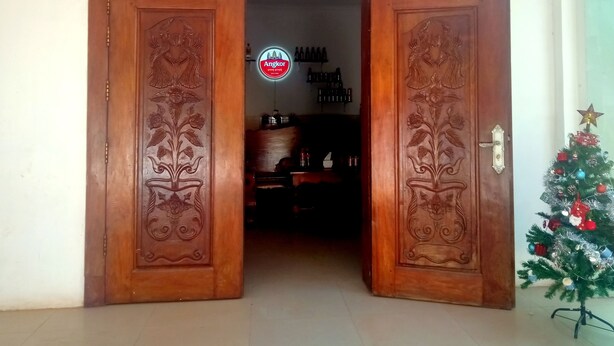 A wooden door with intricate carvings, leading to a room with a Christmas tree and a neon sign. - The Crocodile villa (Siem Reap)