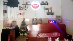 A living room with a wooden sofa, a Christmas tree, and a wall-mounted TV. There are shelves with bottles and cans, and a neon sign. - The Crocodile villa (Siem Reap)