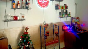 A bar area with shelves of liquor bottles, a neon Angkor sign, and a decorated Christmas tree. - The Crocodile villa (Siem Reap)