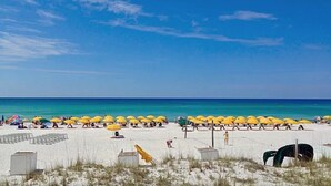 A beach with rows of yellow umbrellas and white beach huts.