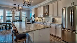 A modern kitchen with a large island, stainless steel appliances, and pendant lighting.