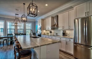 A modern kitchen with a large island, stainless steel appliances, and pendant lighting.