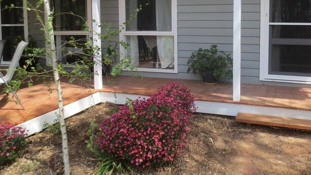 A residential house with a covered porch, large windows, and a small garden with pink flowers.