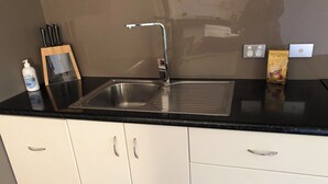 A kitchen with a stainless steel sink, white cabinets, and a black countertop.