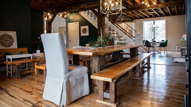 L’intérieur est rustique, avec une table à manger en bois, des bancs et une chaise. Un escalier mène à un niveau supérieur.