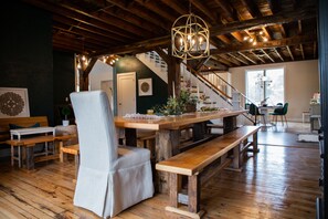 A rustic interior with a wooden dining table, benches, and a chair. A staircase leads to an upper level.
