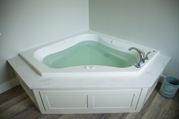 A white freestanding bathtub with a greenish water level, a modern faucet, and a small trash can to the right.