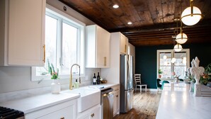 Une cuisine moderne avec des meubles blancs, des appareils en acier inoxydable et un plafond en bois.