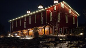 Un grand bâtiment de style grange, de couleur rouge, doté de nombreuses fenêtres et d’une tour horloge, illuminé par des éclairages extérieurs.