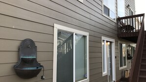Een huis met grijze gevelbekleding, een veranda met een bankje, en een trap die leidt naar een balkon op de tweede verdieping.