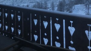 Un balcón con recortes en forma de corazón, con vistas a montañas nevadas y un cielo despejado.