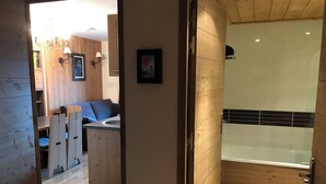 Un baño moderno con tocador de madera, ducha y un pequeño rincón de descanso con mesa y sillas.