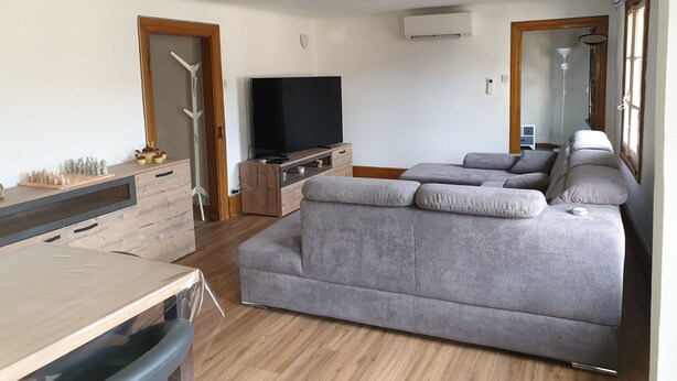 A modern living room with a grey sofa, wooden flooring, a flat-screen TV, and a wooden cabinet.