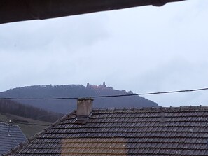 A view of a building with a tiled roof and a chimney, overlooking a hill with a castle-like structure in the distance.