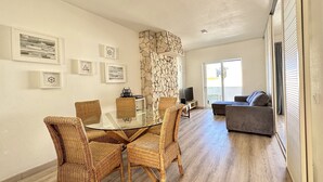 Un salon moderne avec une table à manger au plateau en verre, entourée de chaises en osier, un mur d’accent en pierre et un canapé gris.