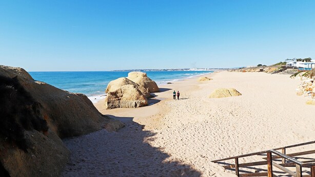 Une plage de sable avec de gros rochers et un ciel bleu dégagé.