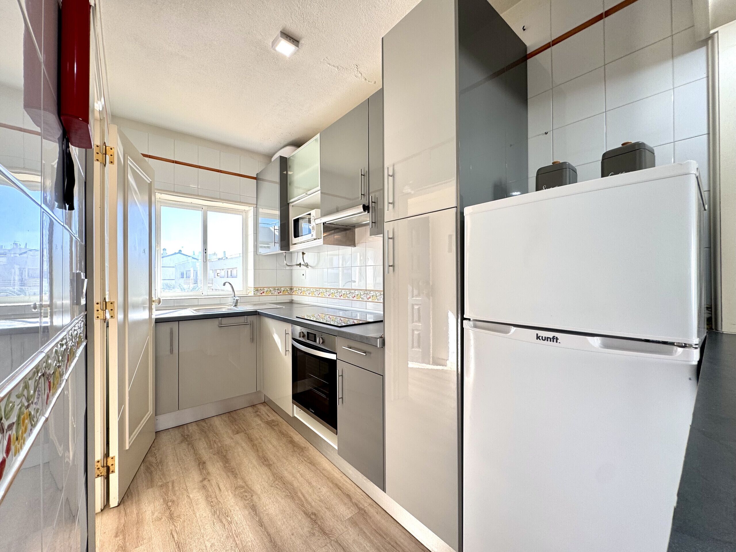 A modern kitchen with white cabinets, a built-in oven, a microwave, and a refrigerator.