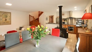 Un coin repas comprenant une table, des chaises et un vase de fleurs. La cuisine est équipée d’une cuisinière et d’appareils électroménagers modernes.