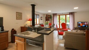 Une cuisine avec un îlot central, un coin repas avec des chaises rouges, un canapé et un téléviseur dans le salon.